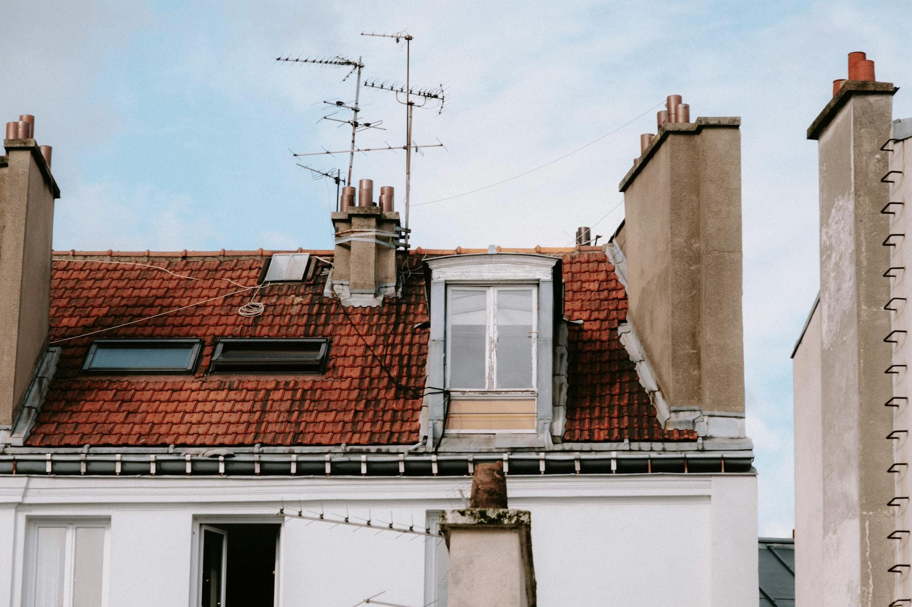 A quaint urban rooftop with chimney and antennas, capturing architectural details and city vibe.