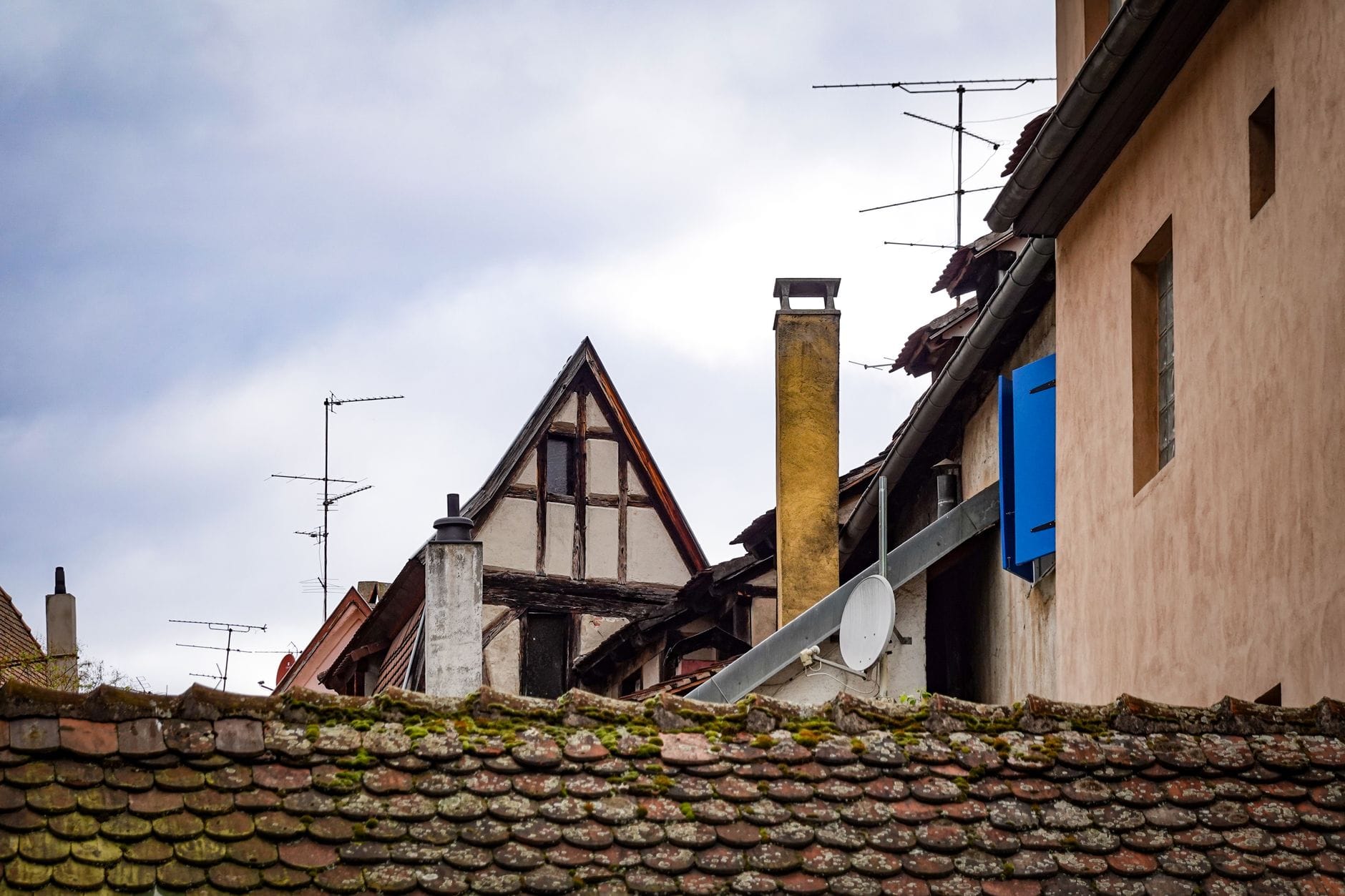 Rustic rooftops and chimneys of old European buildings with a cloudy sky.