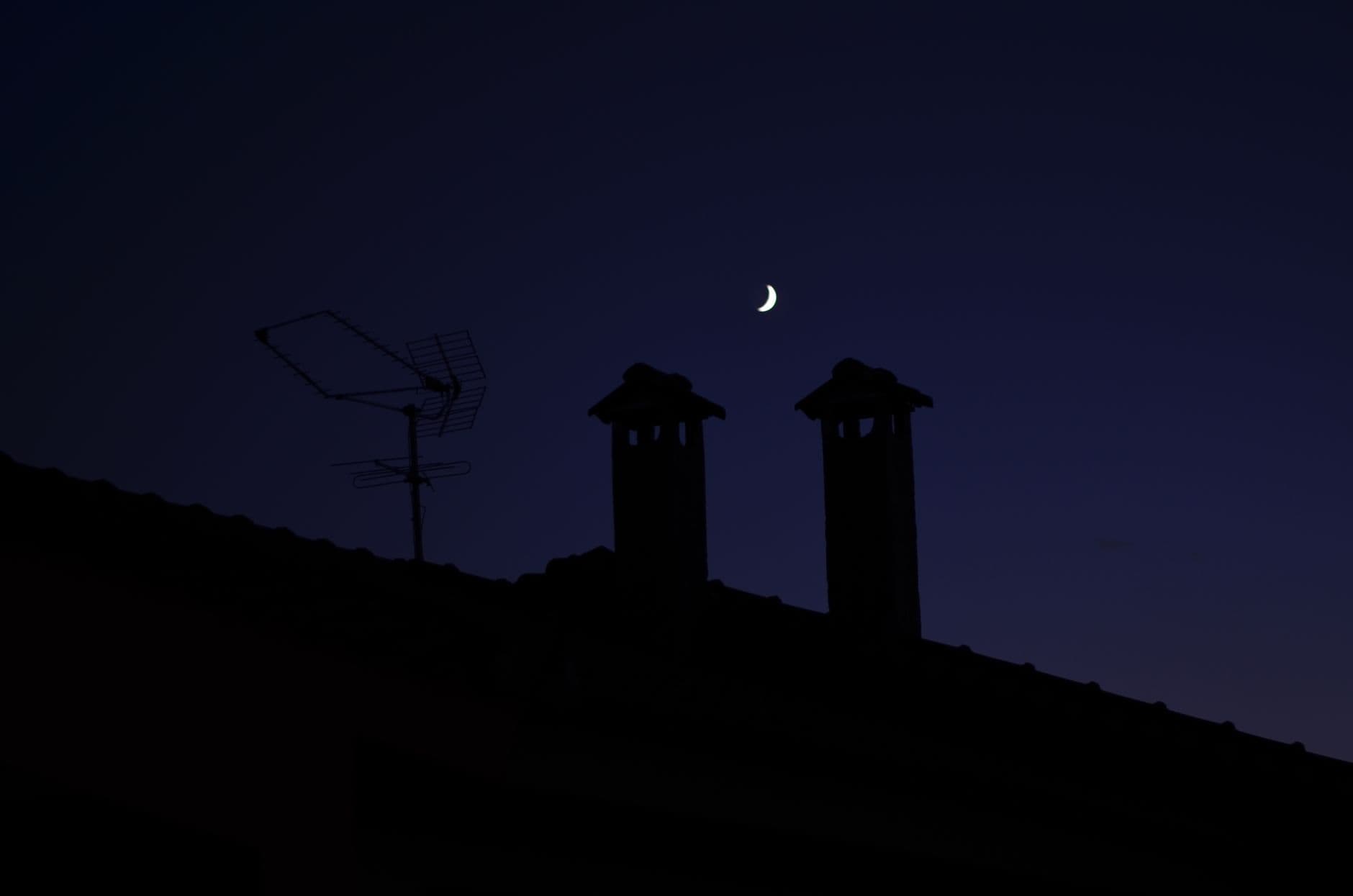 A serene night sky over Greek rooftops with crescent moon and silhouettes.